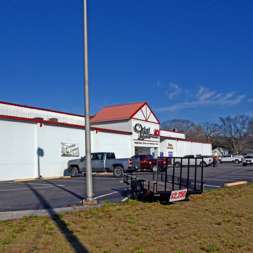 Parking lot in front of a white and red Ace hardware store under a clear blue sky. Trucks are parked, and a trailer is for sale at $2,250.